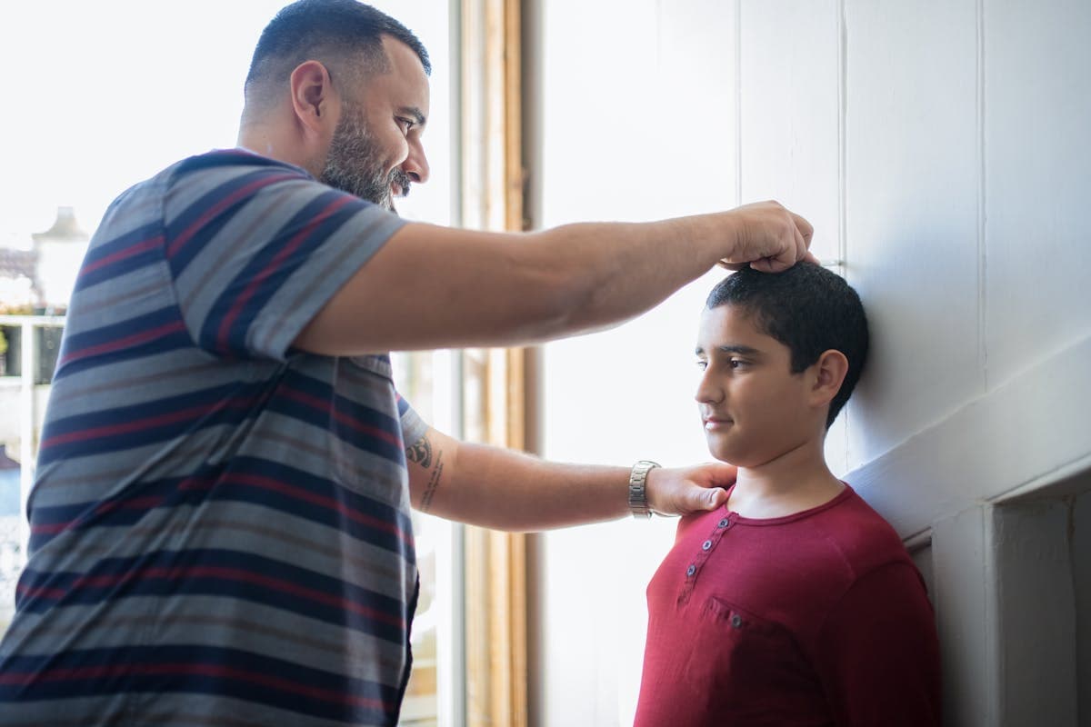 A parent measuring a child at home with a soft tape measure, casual and relaxed setting
