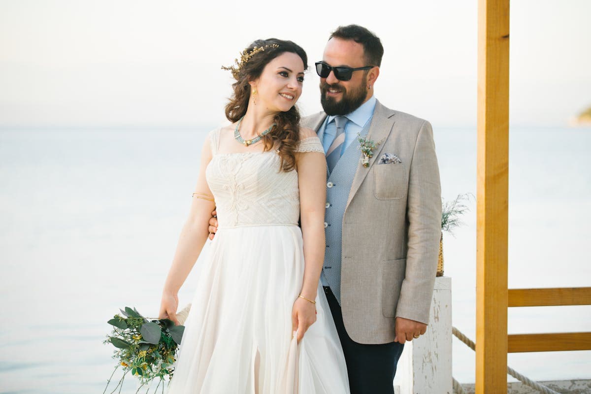 Bride in a flowing silk gown beside a groom in soft linen on a beach, their fabrics matching in visual softness for the photograph