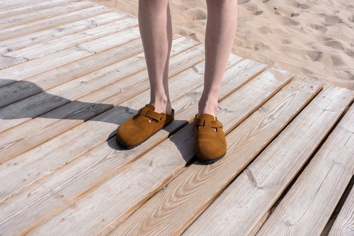 Flat suede loafers and woven jute-soled espadrilles arranged on sand, the kind of low-profile footwear that does not sink at a beach ceremony