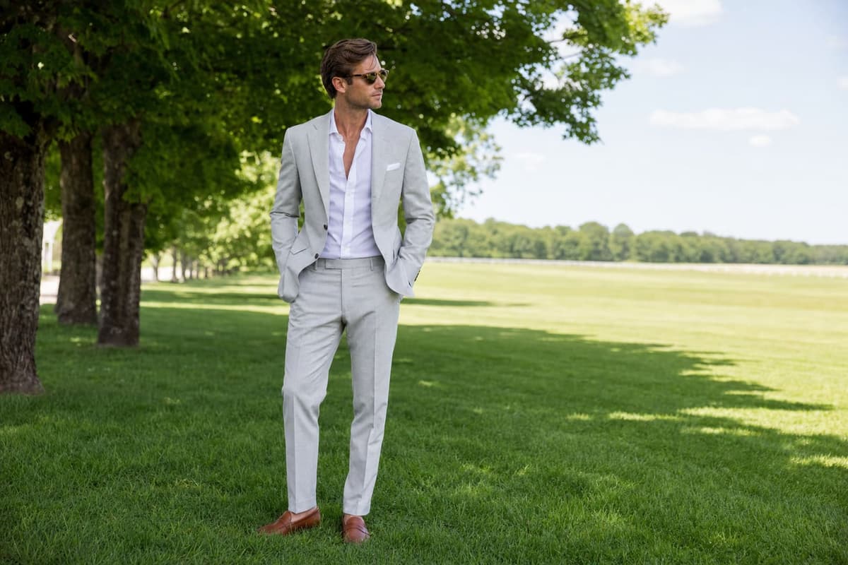Man in a light stone-grey summer suit on a green lawn -- the refined Saratoga summer aesthetic for the Belmont Stakes