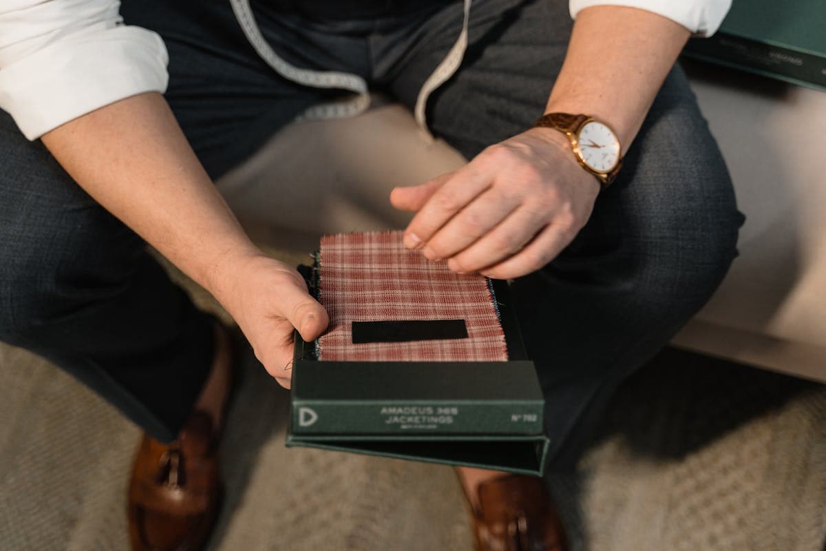 Hands flipping through stacked wool suiting fabric swatch books to choose a cloth for a made-to-measure suit