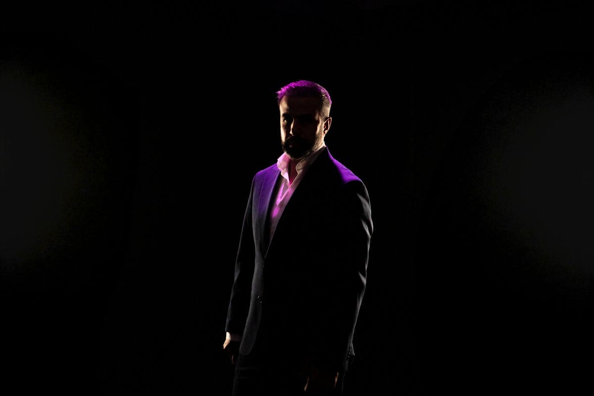 Groom in a dark aubergine purple suit photographed in dim evening light where the suit reads almost black with hints of purple