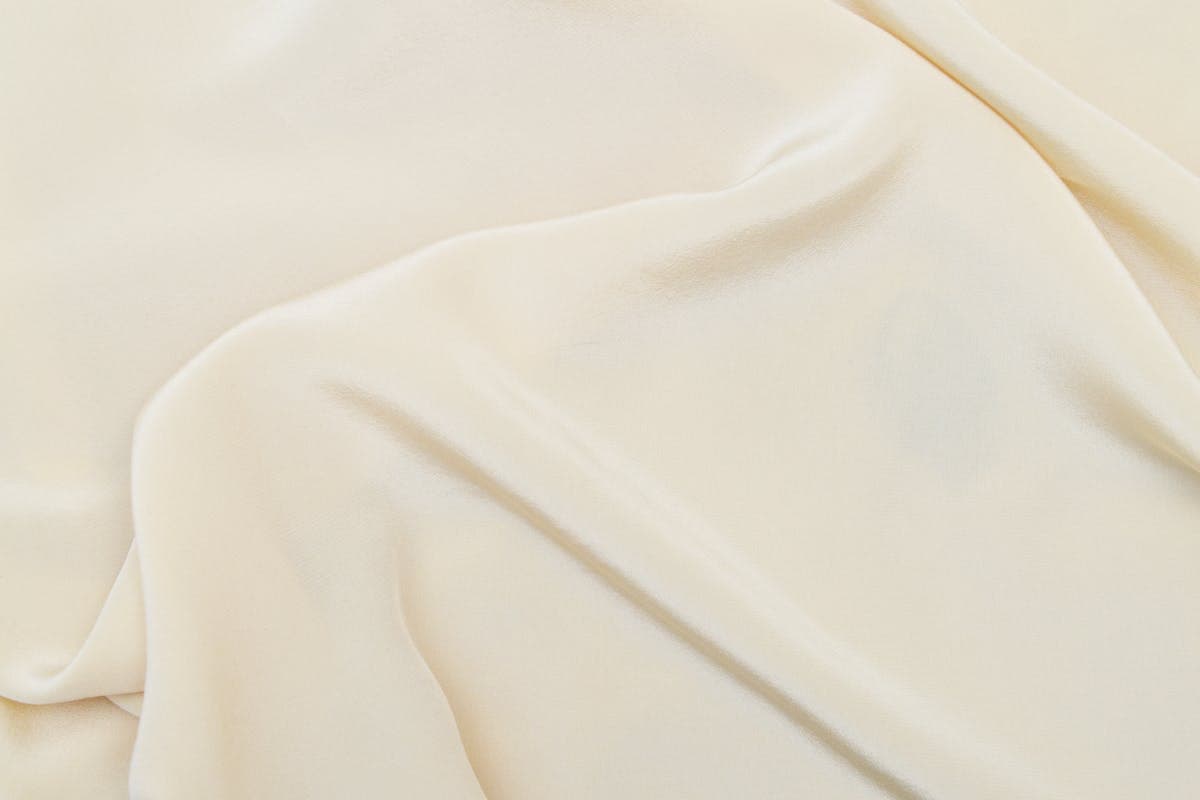 Folds of pearl-white crepe silk and charmeuse fabric showing matte and glossy finishes, the materials used for a custom CBK-style dress