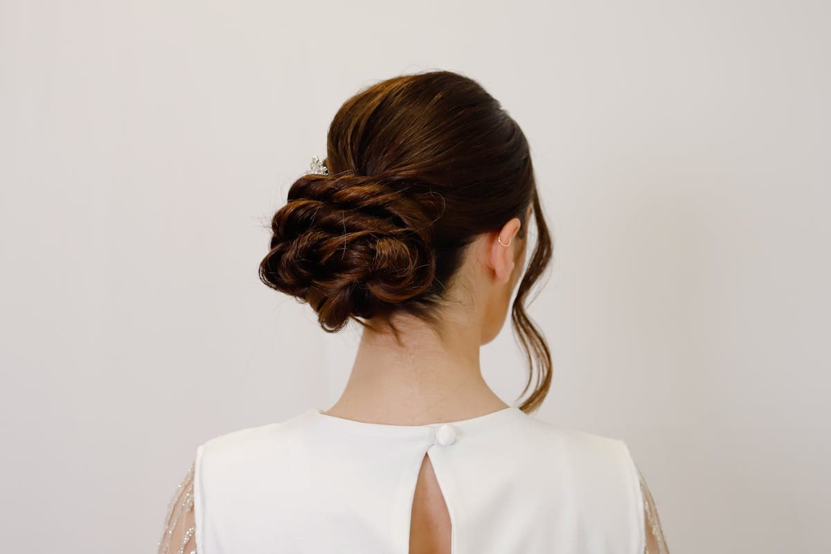 A bride styled in the restrained CBK aesthetic: sleek center-parted updo, bare-faced makeup, a simple tulle veil and a small white bouquet