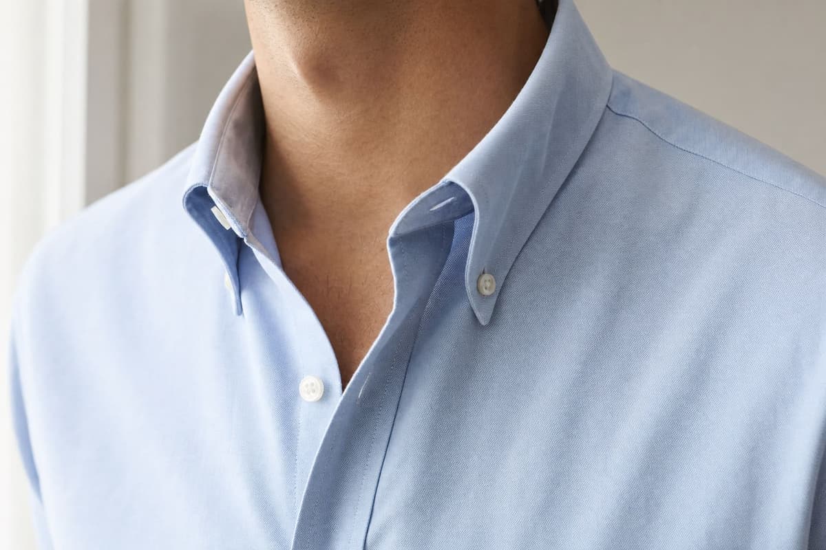 A light blue oxford cloth button-down shirt collar with a soft roll, worn open at the neck