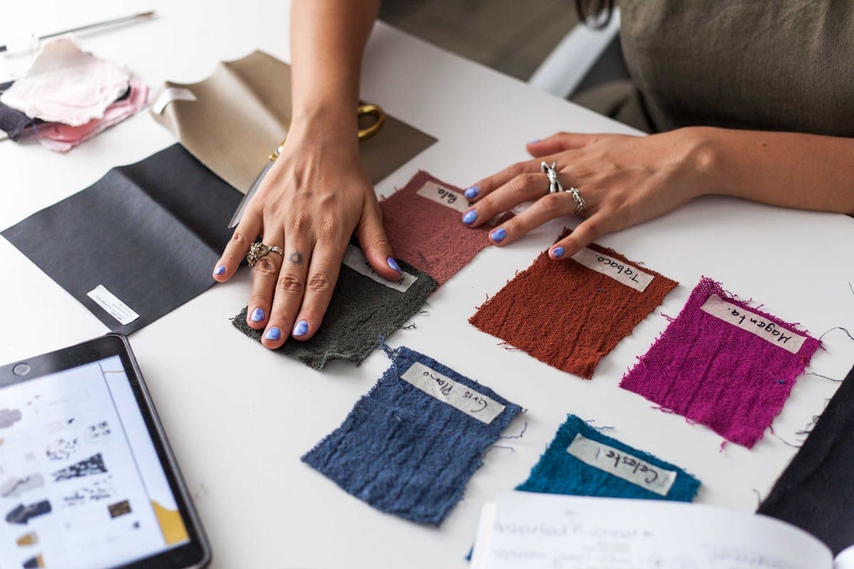 Hands comparing fabric swatches and lace samples laid out on a table