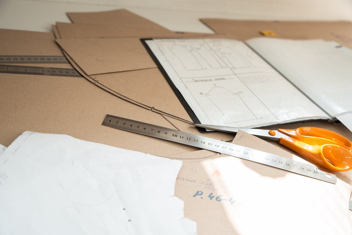 Hands drafting a garment pattern on paper with rulers and a pencil on a worktable
