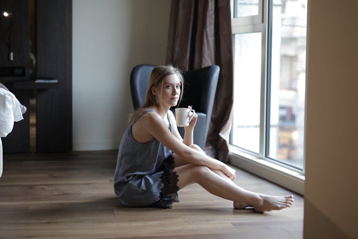 Woman in silk pajamas in soft morning light with coffee, capturing the aspirational that-girl morning routine aesthetic