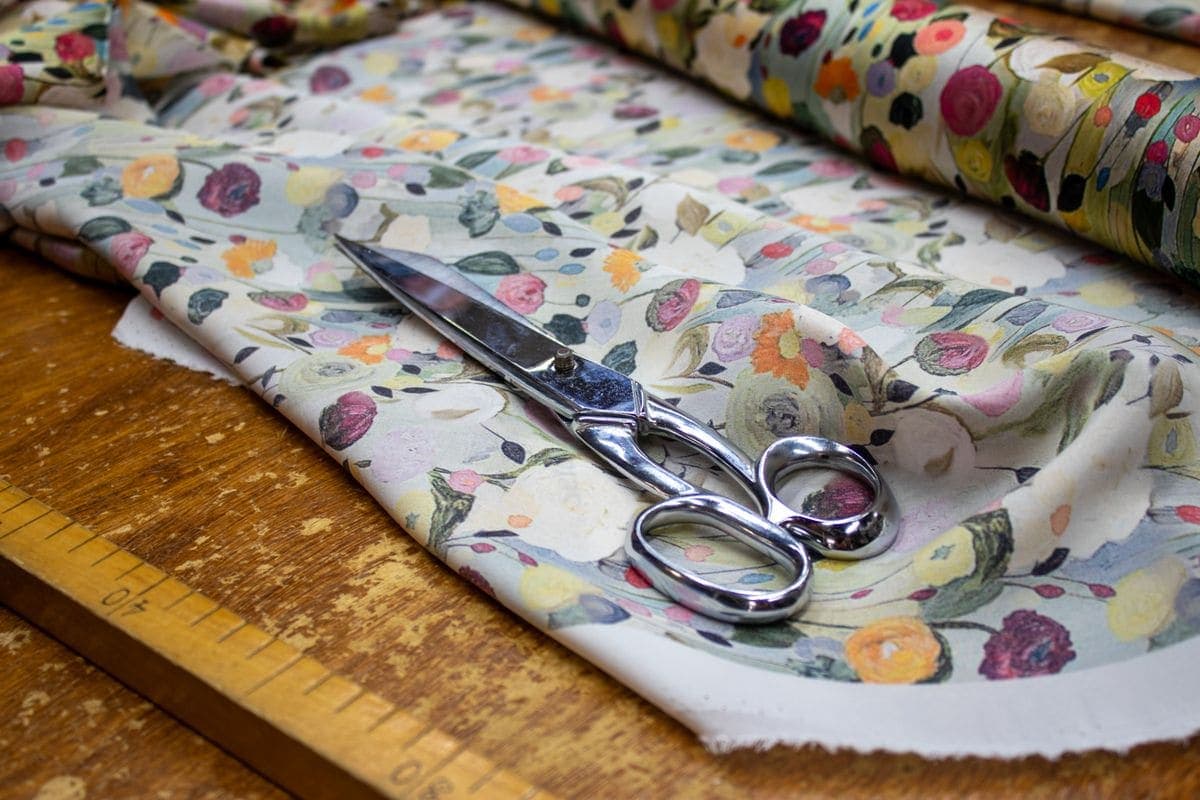 Tailor's hands cutting and pinning fine silk fabric on a workshop table, illustrating made-to-measure pajama construction