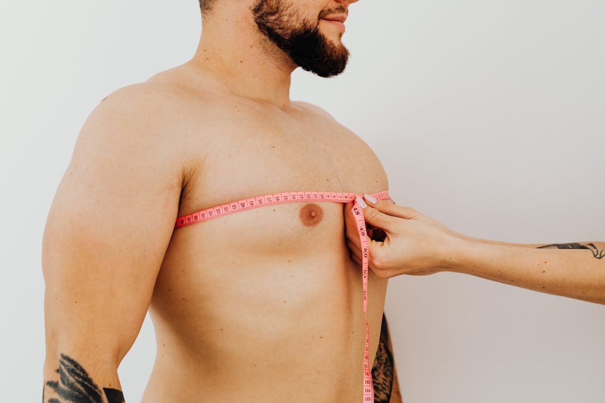 Person measuring their own chest with a yellow tape measure while following guidance on a phone propped nearby