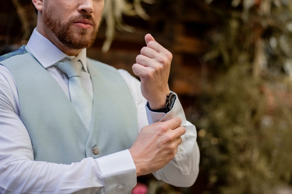 Groom in a well-fitted navy custom three-piece suit adjusting his cuff before a wedding