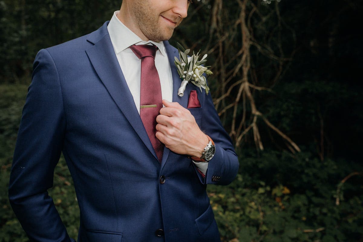 Groom standing in a deep navy double-breasted wedding suit photographed in warm evening light