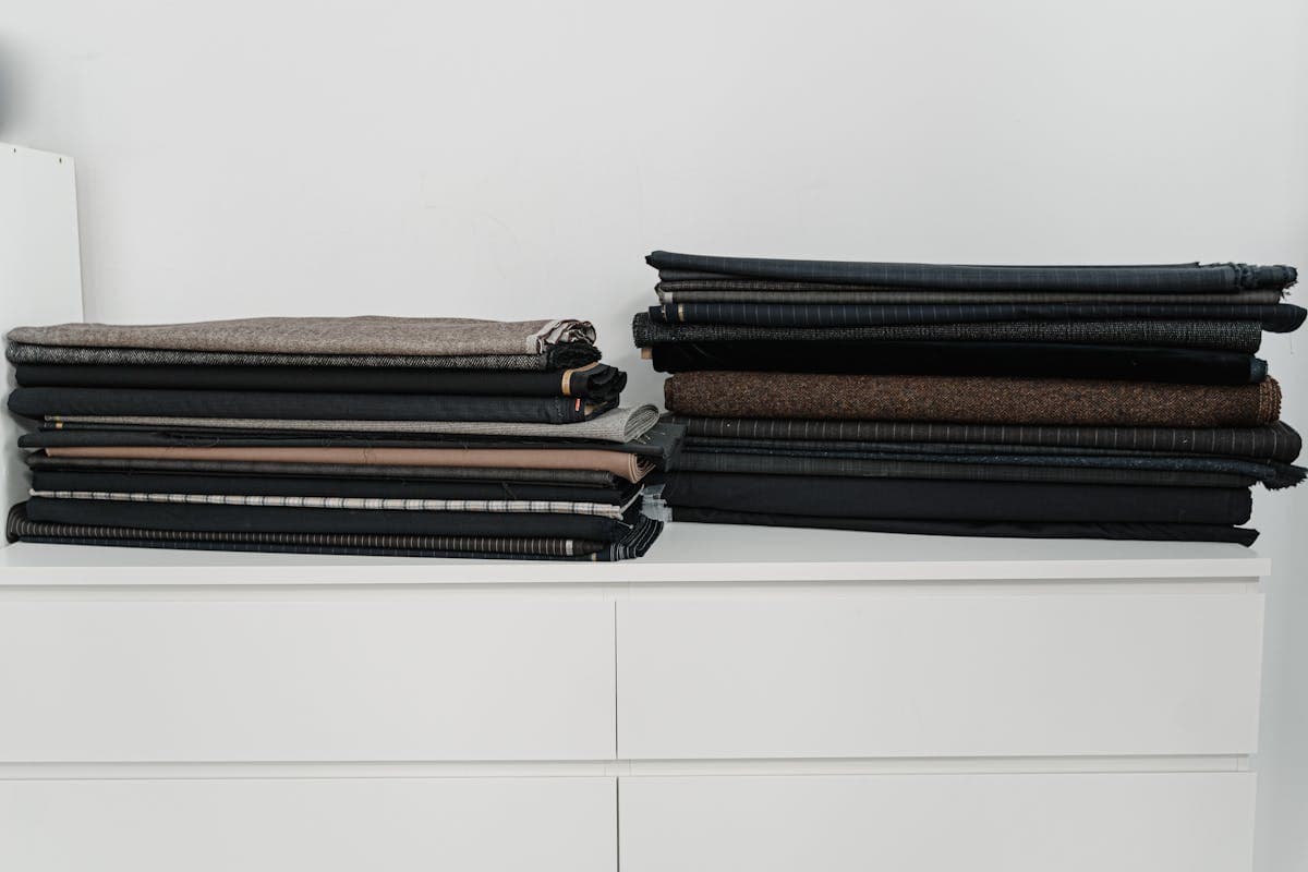 Stacked and rolled wool suiting fabric swatches in navy, charcoal and burgundy tones with visible texture