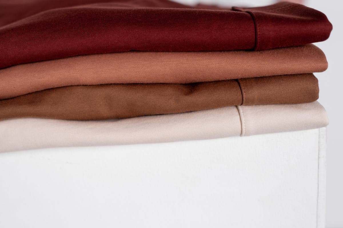 Stacked and folded wool, tweed and wool-silk fabric bolts in tobacco, moss, oxblood and navy tones laid out for selection