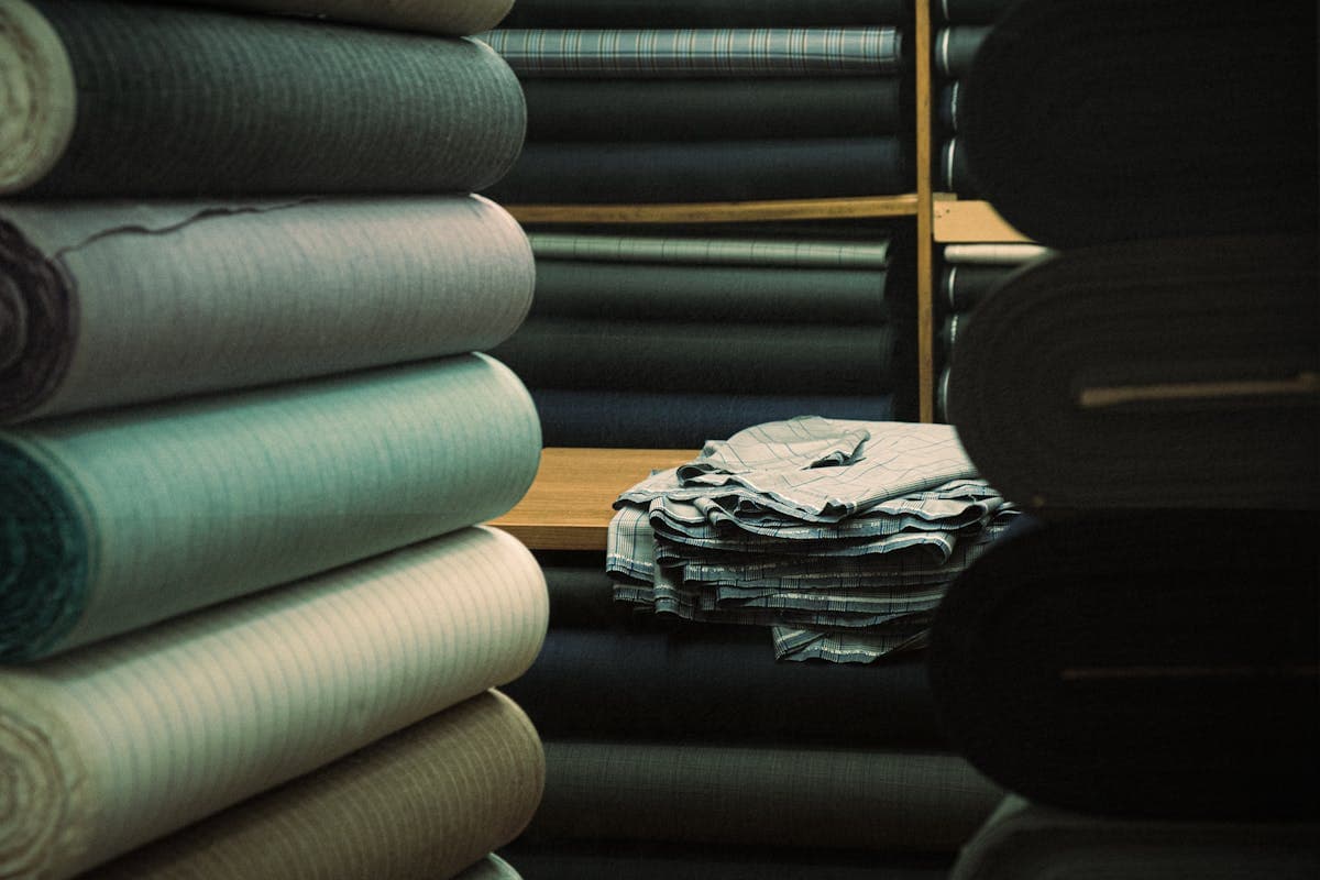 Folded bolts of Italian and English wool suiting cloth in charcoal and navy on a tailor's table