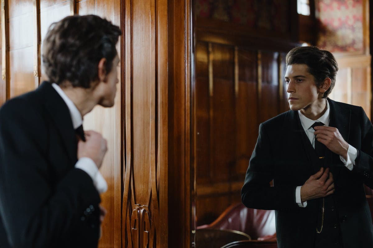 A man adjusting his jacket in front of a mirror with a quiet, satisfied expression -- the calm confidence of clothes that finally fit