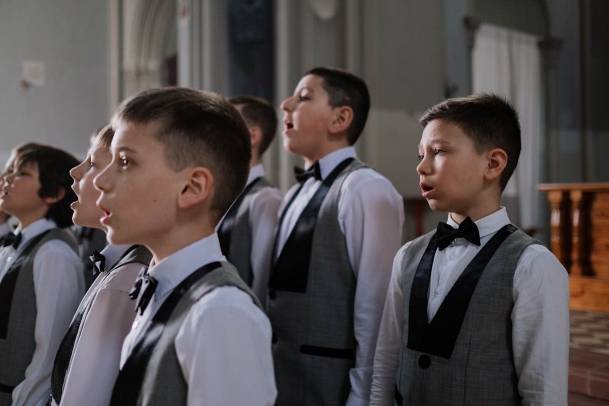 Children walking into a stone church for a First Communion ceremony, boys in dark suits among the group