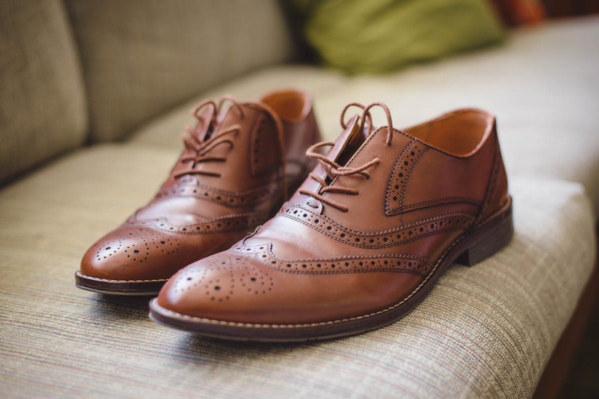 Pair of dark brown leather oxford dress shoes beside a matching brown leather belt on a neutral surface