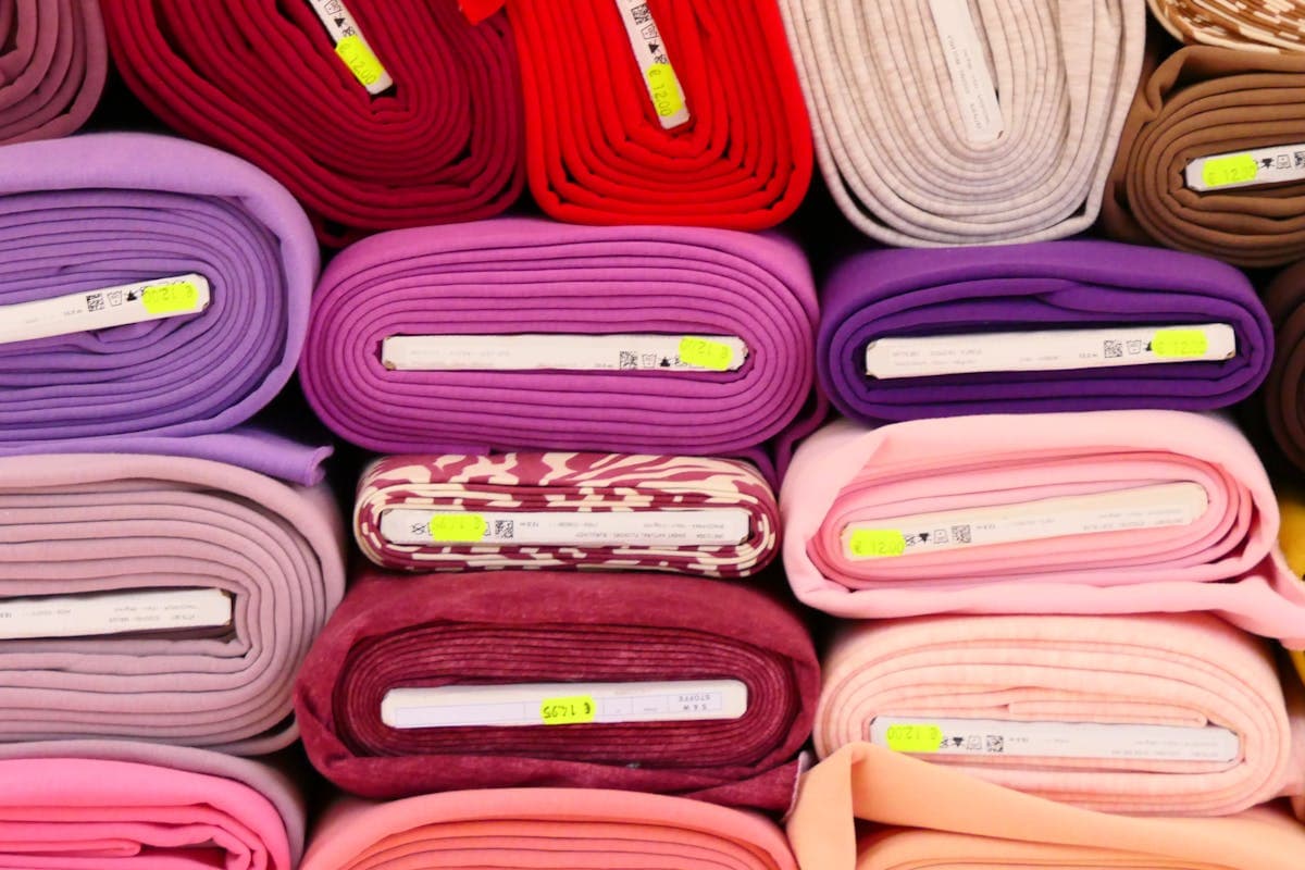 Wall of stacked fabric bolts in many colors and textures — wool, linen, cotton and silk — at a Hoi An tailor shop