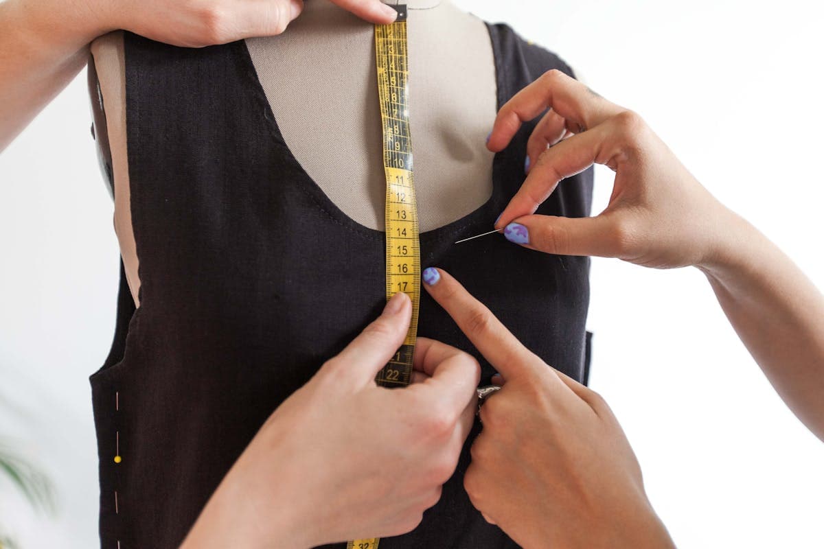 Tailor's hands pinning the lapel of a jacket on a dress form during construction, illustrating the hand-work behind the price