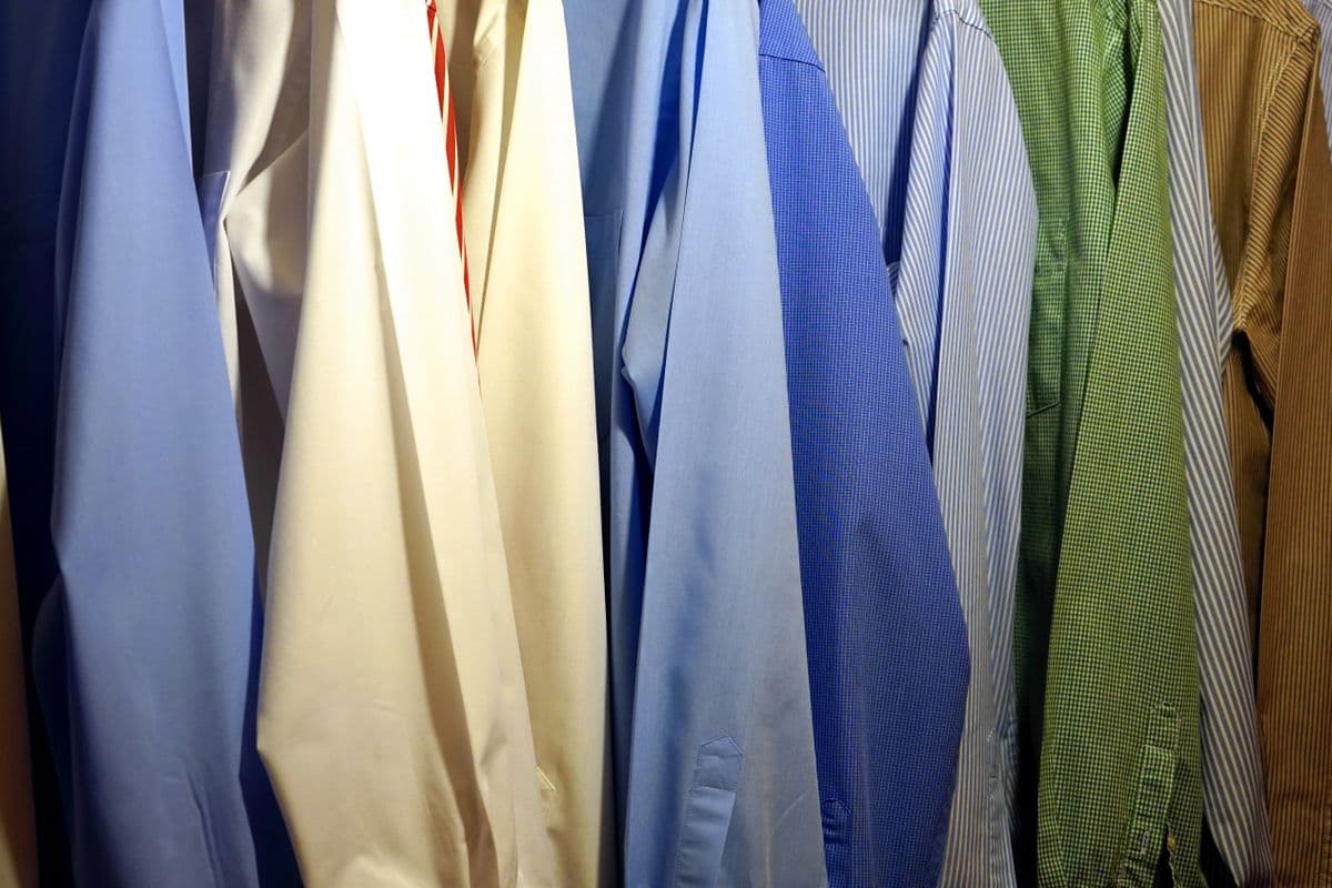 A row of identical white dress shirts pressed and hanging on a rack, ready for another work week