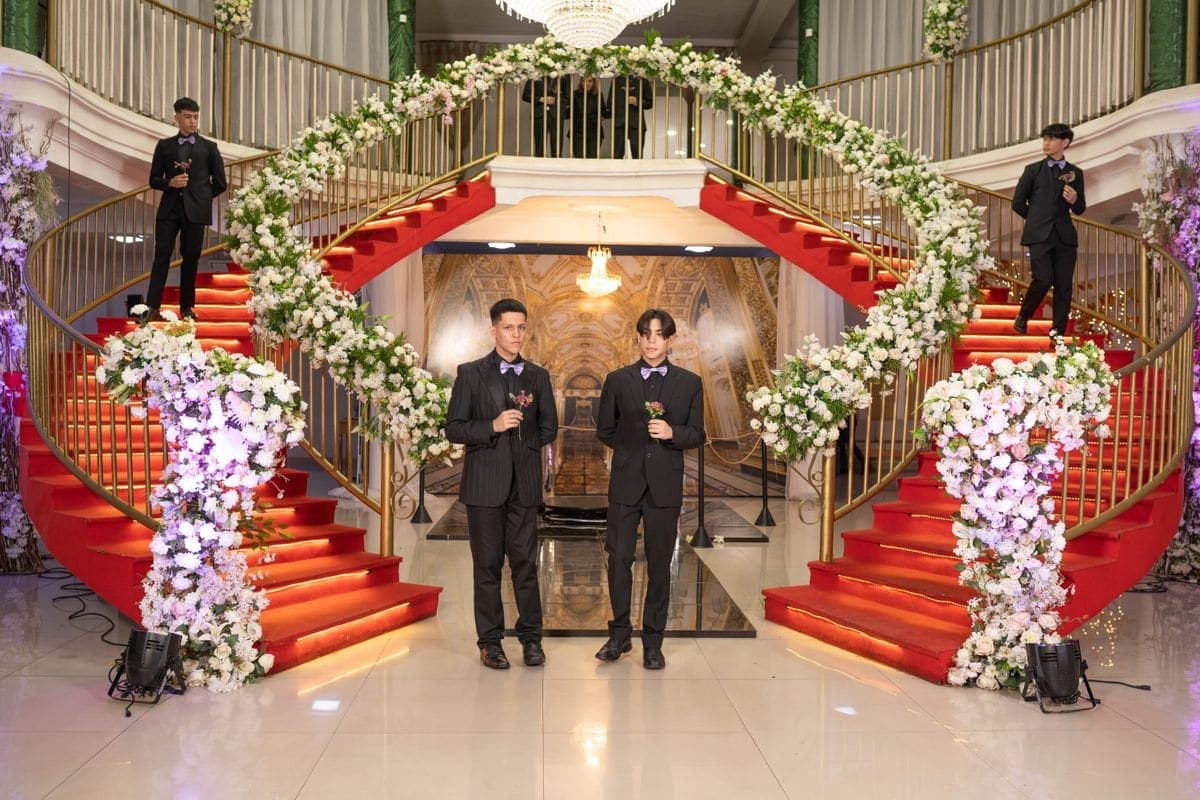 Groomsmen in dark formal suits standing in a grand architectural venue with stone columns.