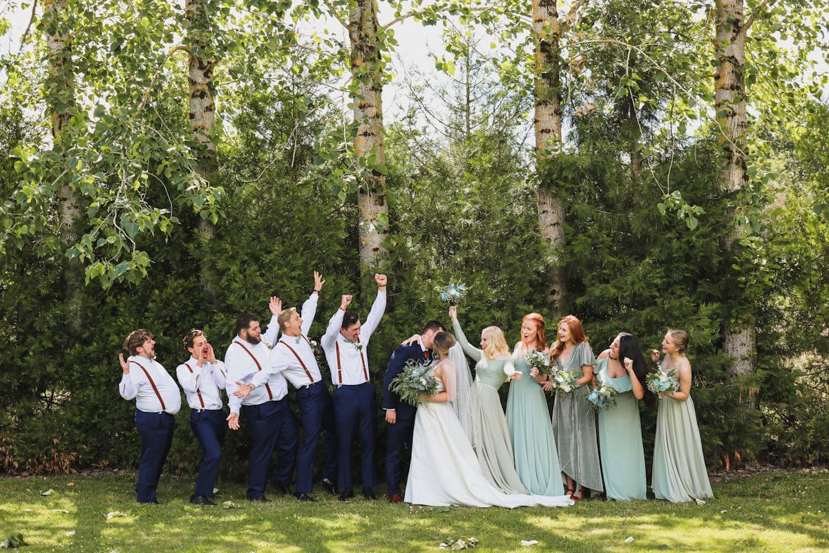 A wedding party of groomsmen in soft sage and earth-tone suits standing outdoors at golden hour.