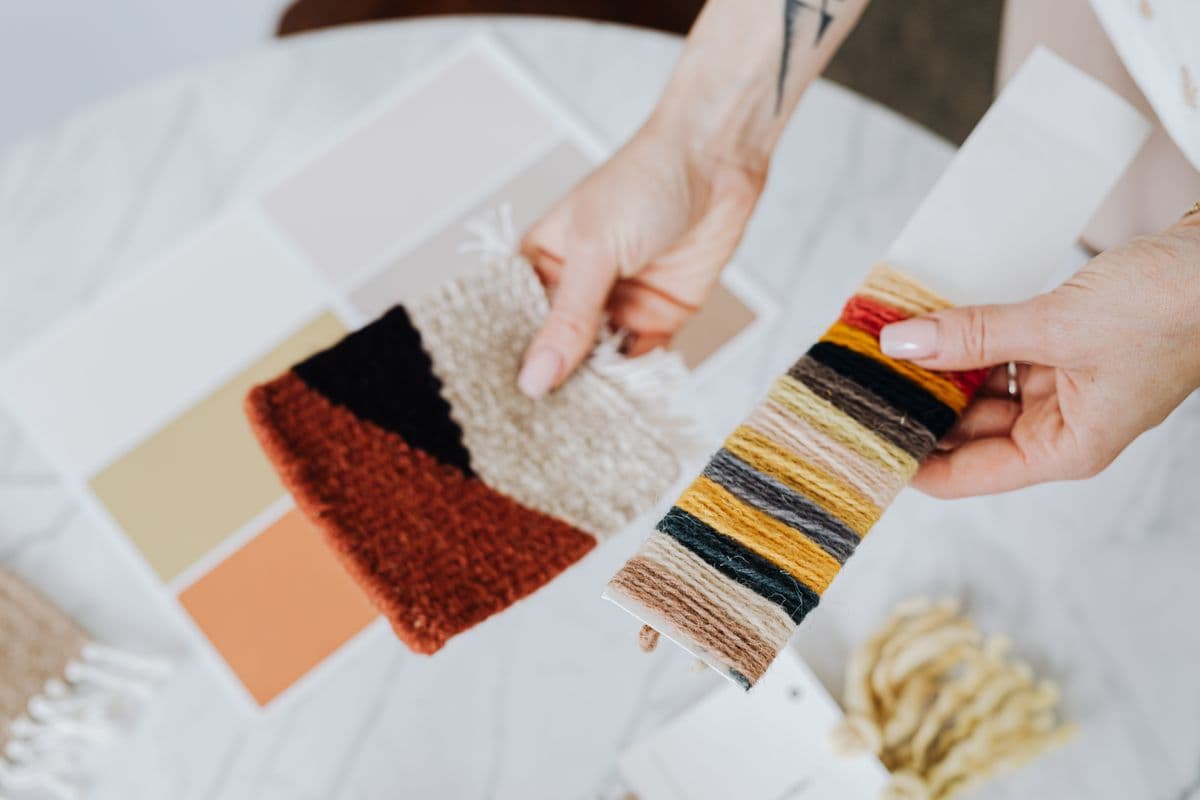 Hands comparing folded wool fabric swatches next to a phone showing a video call