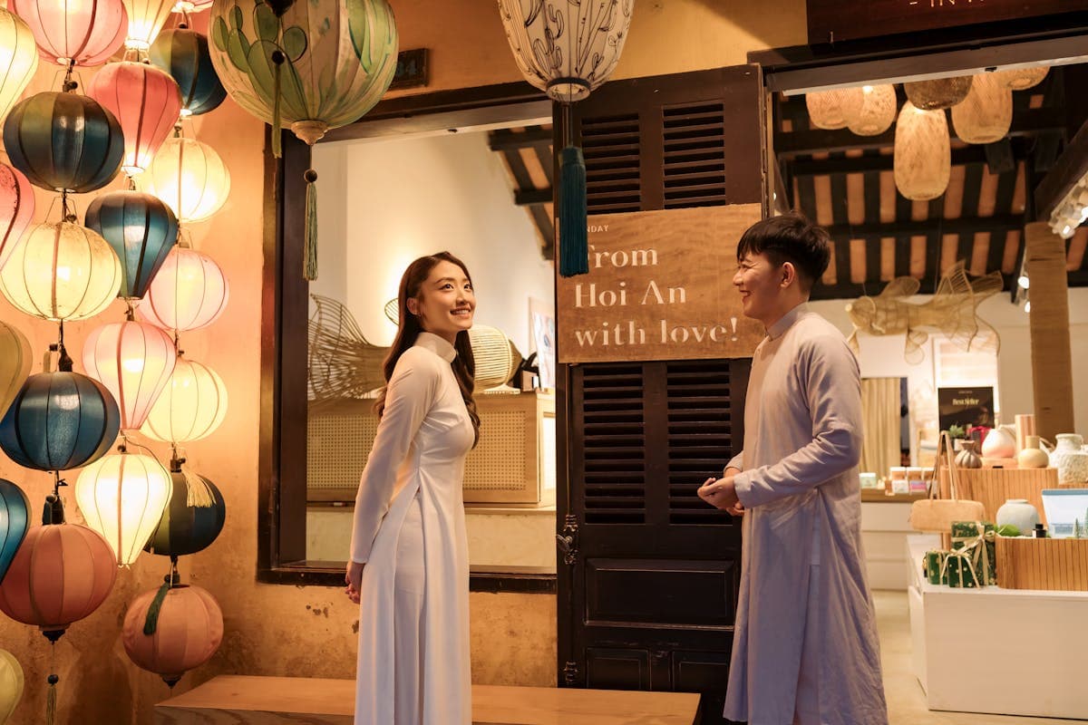 Couple in traditional Vietnamese ao dai posing against the yellow ochre walls of Hoi An Old Town in soft morning light