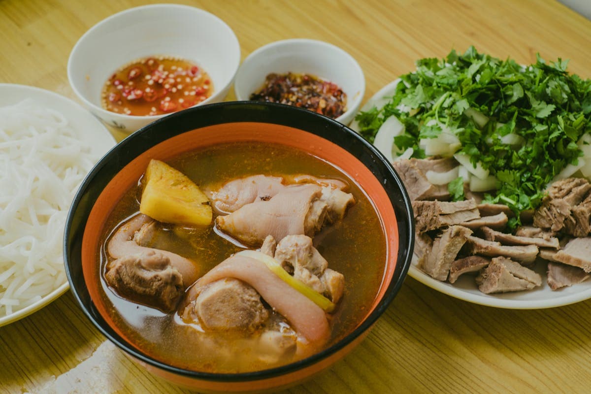 Bowls of cao lau and fresh Vietnamese spring rolls on a table with herbs and chopsticks