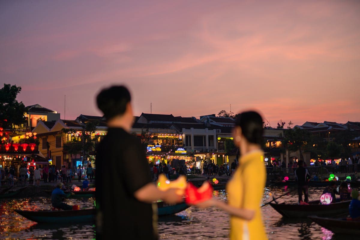 A young child holding a glowing paper lantern by the river in Hoi An at dusk