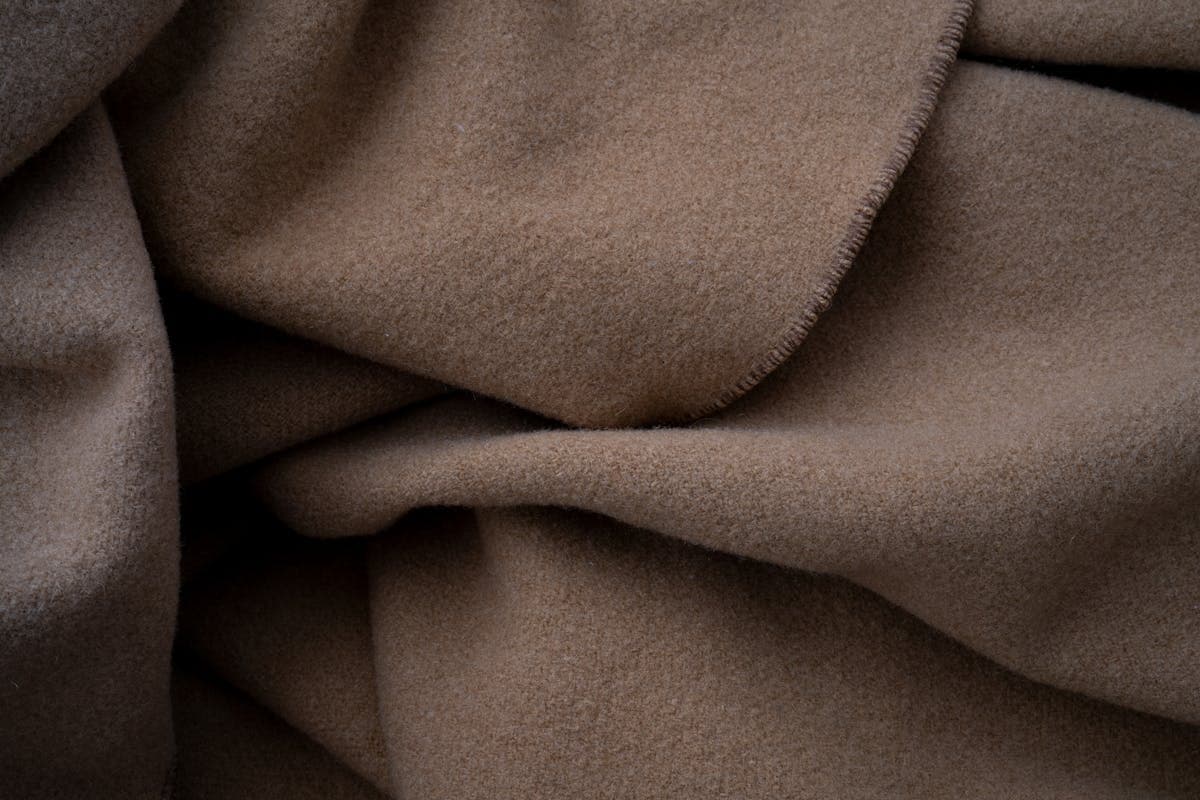 Close-up of soft folded cashmere and wool suiting fabric showing the fine fuzzy fiber texture you check by hand in a Hoi An tailor fitting room to tell real cashmere from synthetic imitations