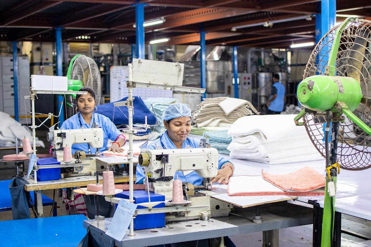 Rows of industrial sewing machines and workers in a large garment factory