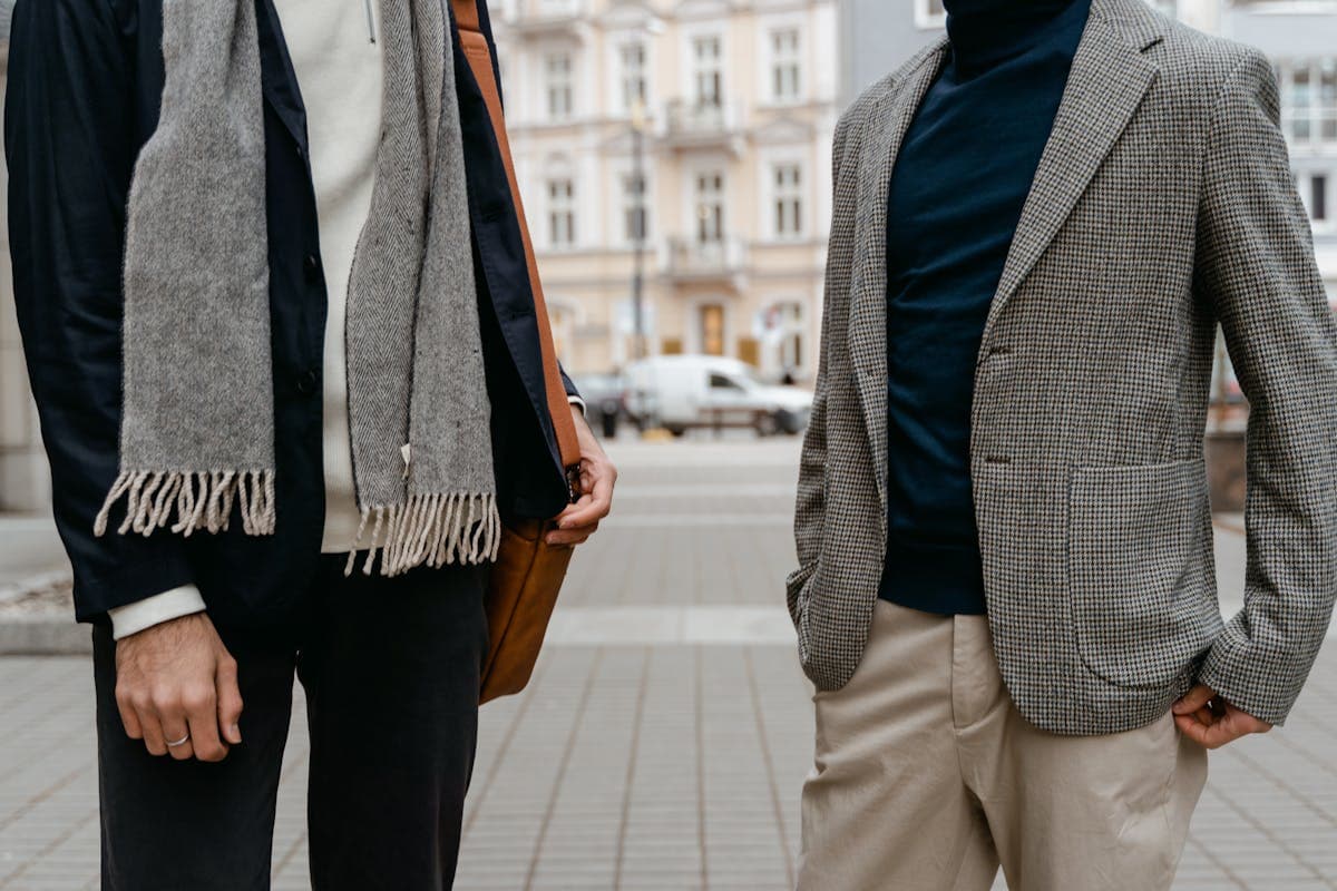 Young man in a navy blazer and chinos with open collar next to a young man in a full matching charcoal suit and tie