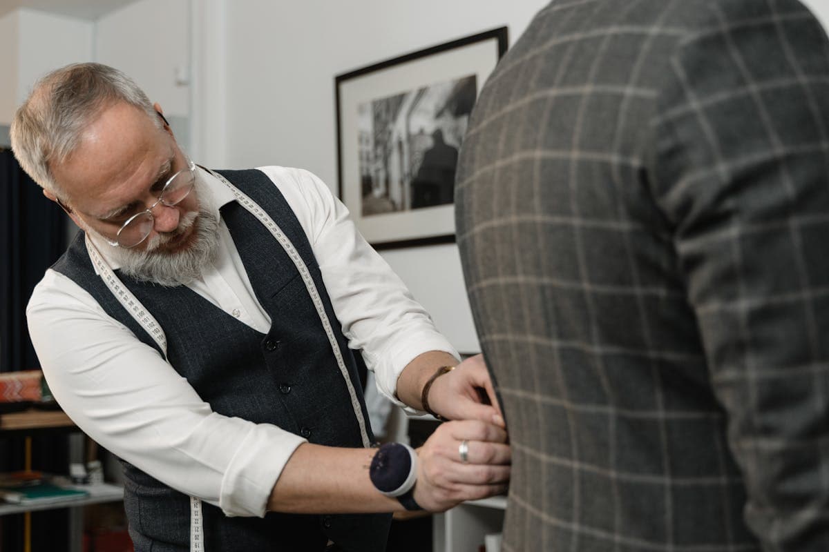 Tailor pinning the shoulder and back of a suit jacket on a customer during a fitting