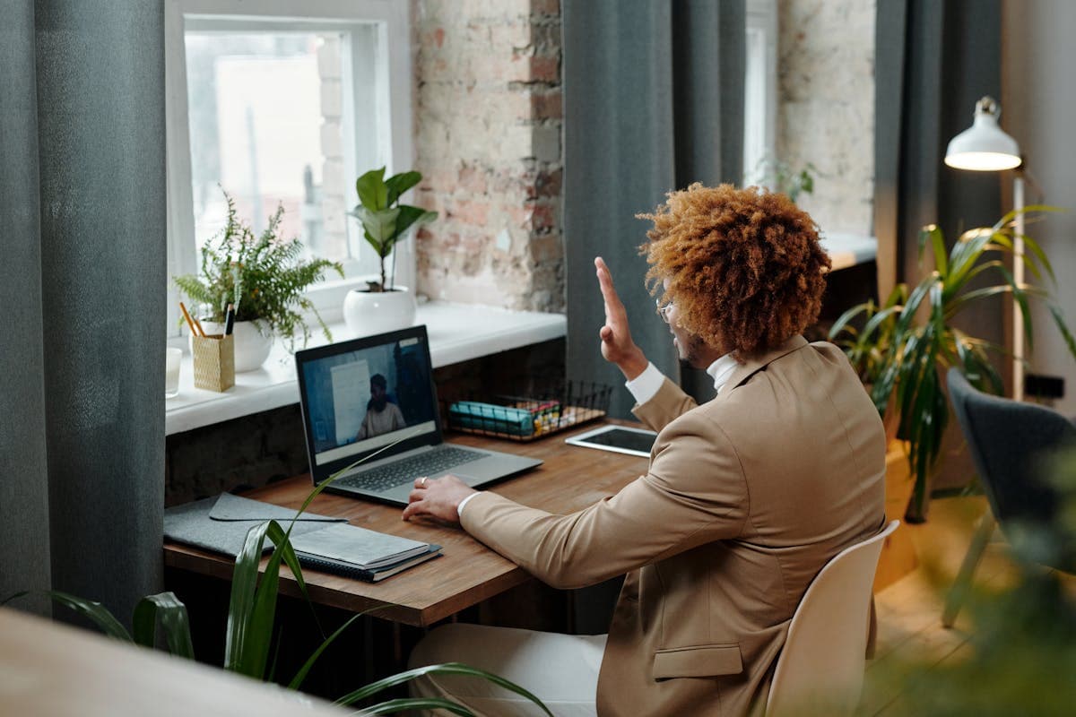Man in a blazer and structured collar shirt sitting at a desk during a video call on a laptop