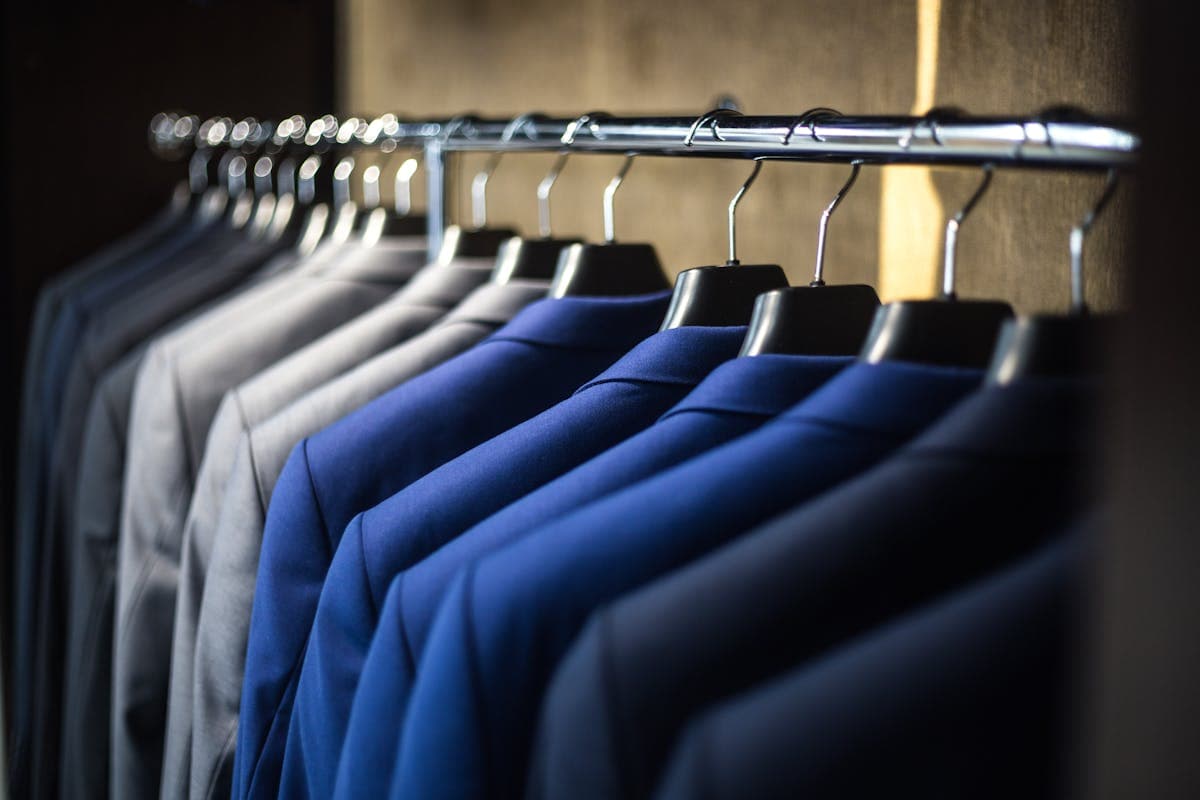 A rack of off-the-rack suit jackets in grey and navy hanging in a clothing store