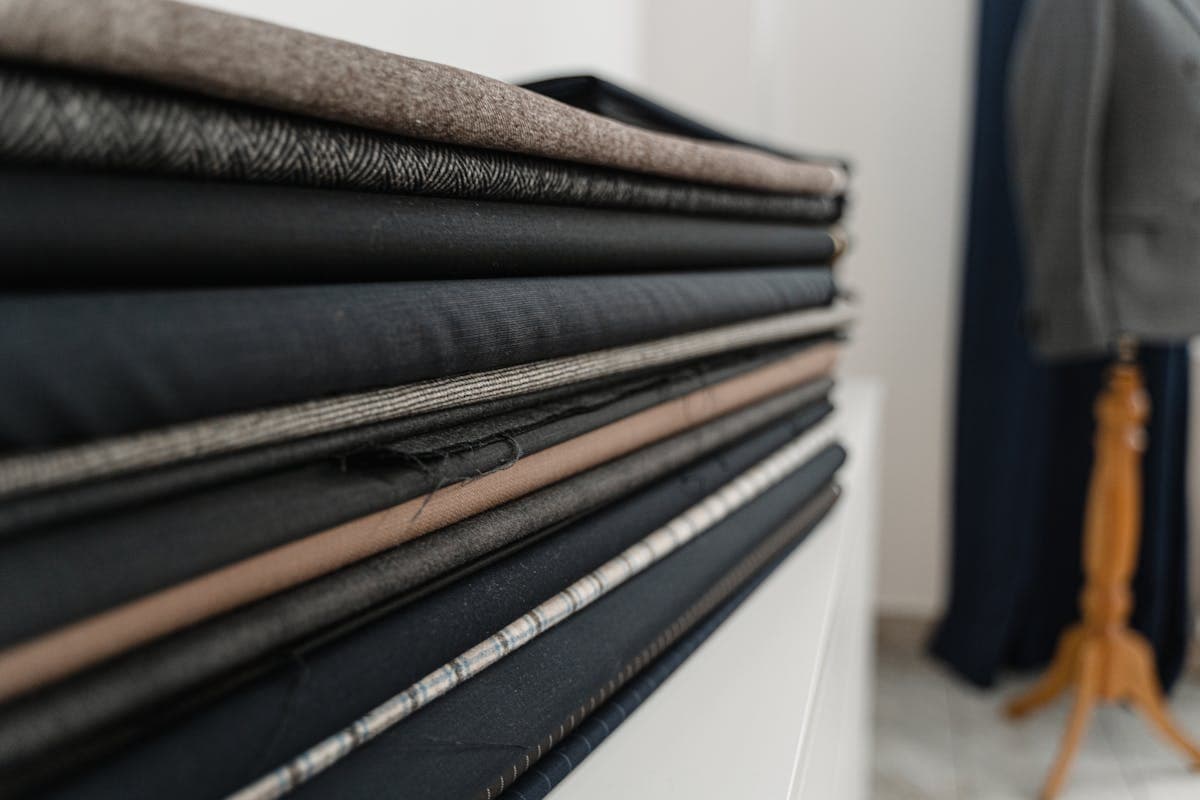 A stack of folded wool suiting fabrics in greys, navy and pinstripe at a tailor shop