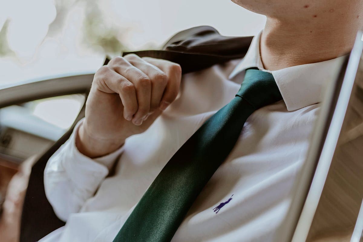 A man wearing a forest green or burgundy wool suit with a tie standing outdoors in spring light
