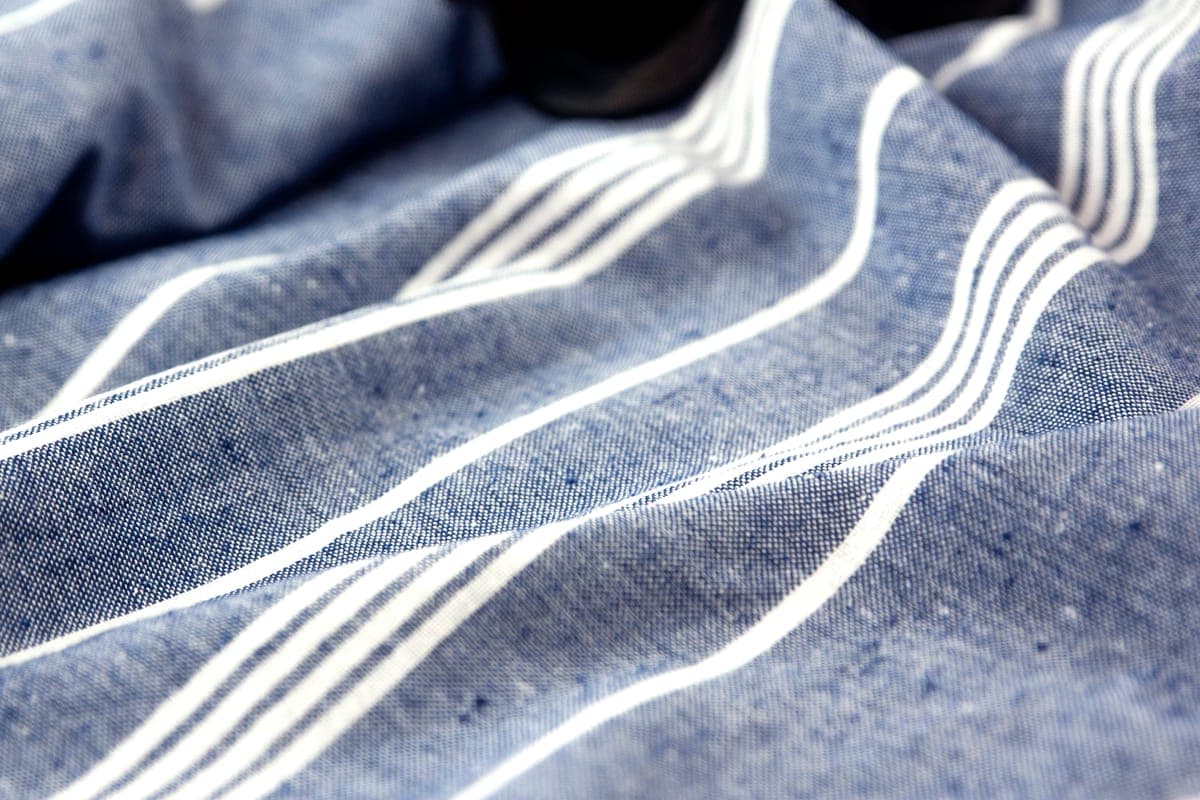 Folded seersucker and pale linen suit fabrics in blue-and-white stripe and sand tones laid out on a table