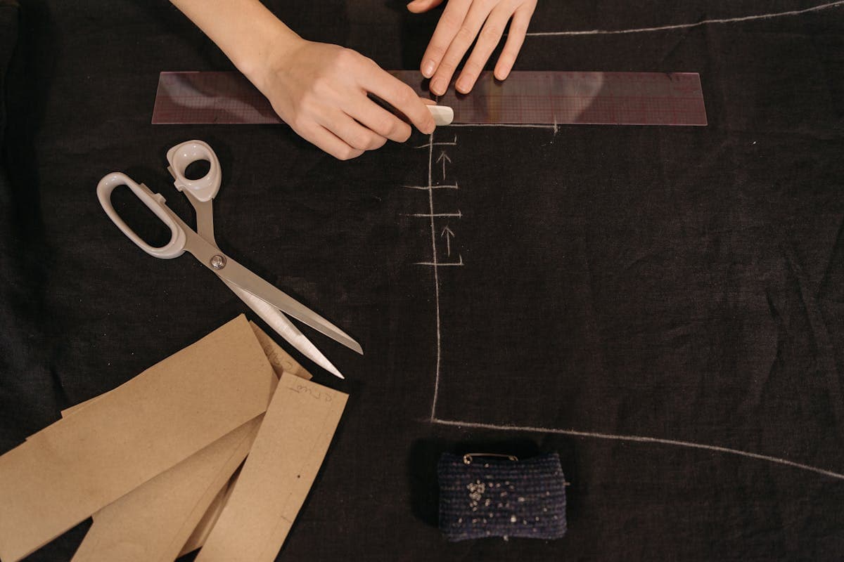 A tailor hand-cutting pale linen suit cloth with chalk and shears on a workshop cutting table