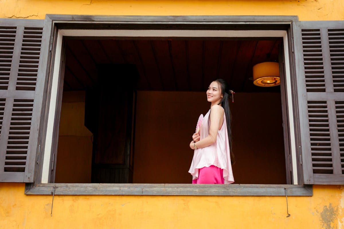 Woman in a bright ao dai standing against the iconic mustard-yellow walls of Hoi An Old Town in golden afternoon light