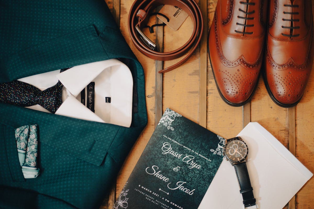Flat lay of men's formal accessories including silk tie, folded pocket square, and a boutonniere