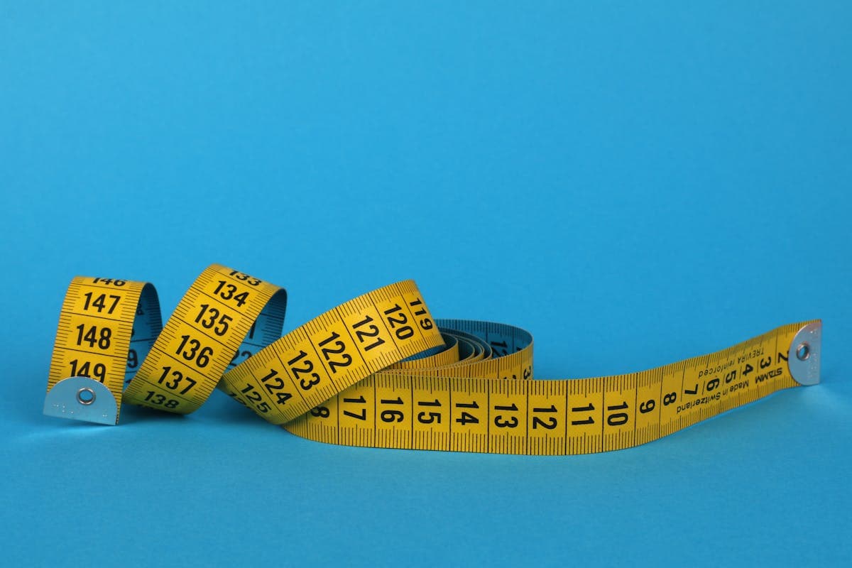 Soft cloth tailor tape measure coiled on a wooden surface beside a notebook and pencil