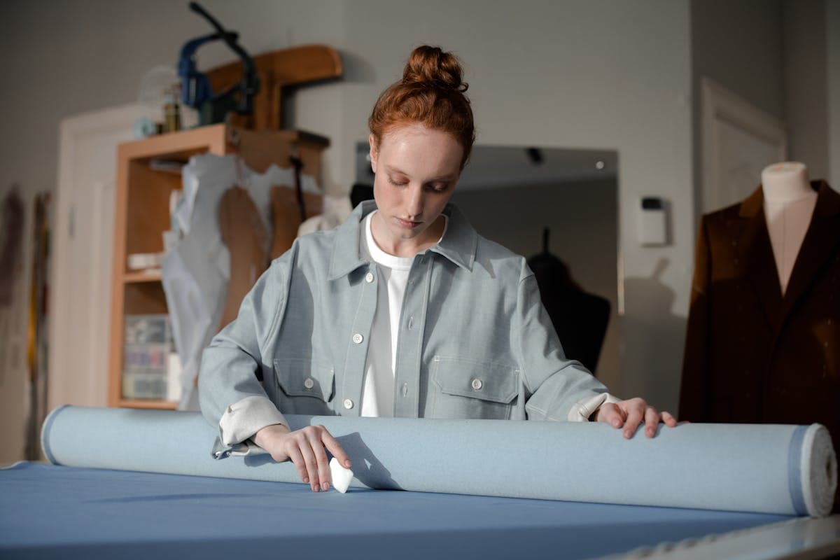 Hands marking a chalk line and tape measure across a half-made jacket on a workbench during a custom suit fitting