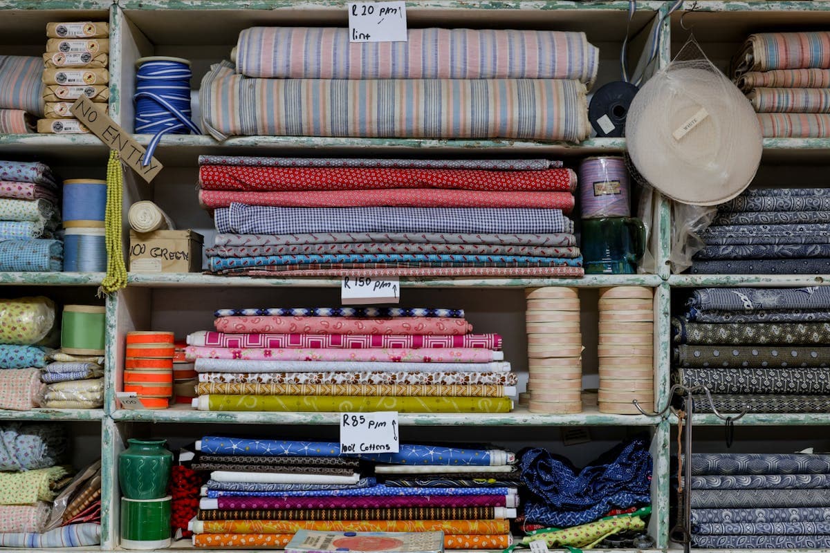 Shelves of folded wool suiting fabric bolts in a tailor workshop, the kind of cloth selection available at Nathan Tailors in Hoi An