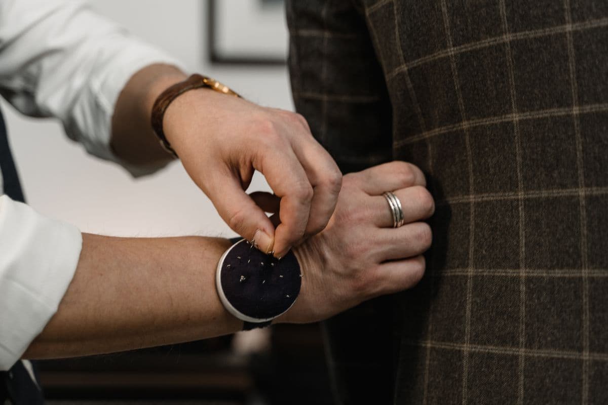 Close-up of a suit jacket shoulder and lapel being pinned during a fitting