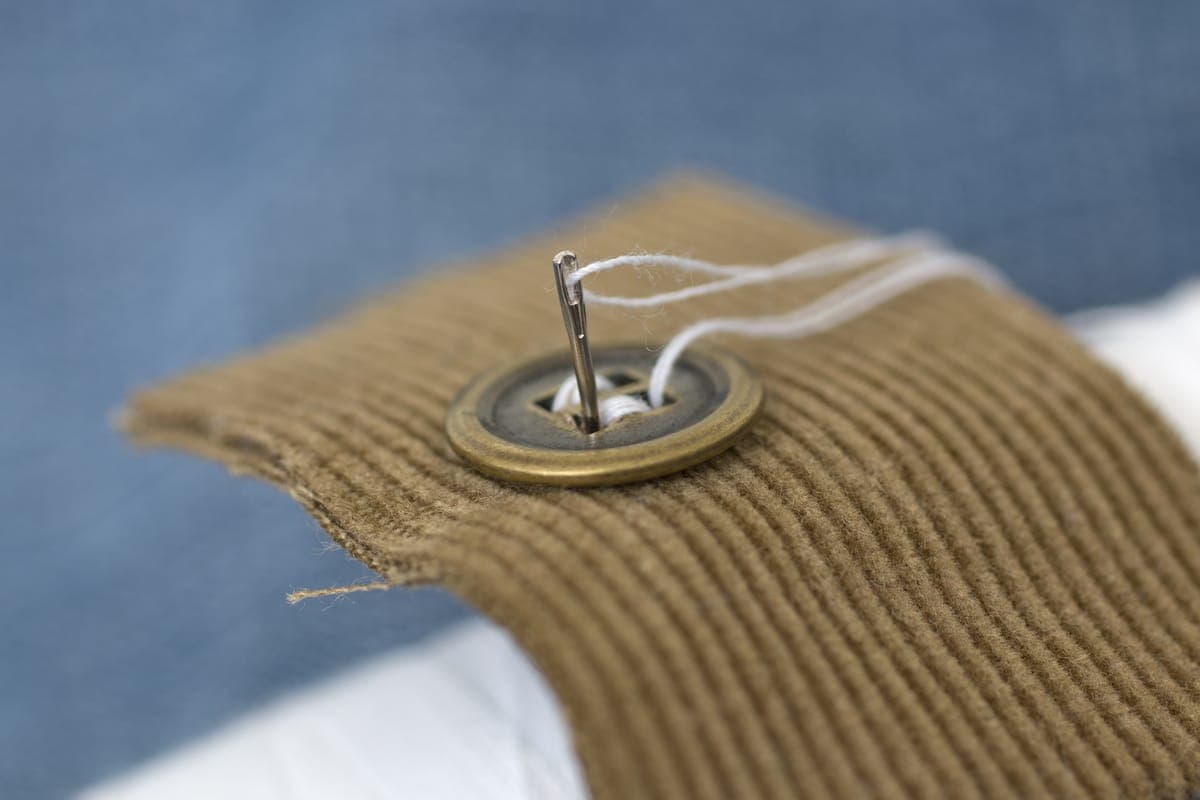 Close-up of a hand needle and thread pad-stitching a layer of canvas into a jacket chest piece