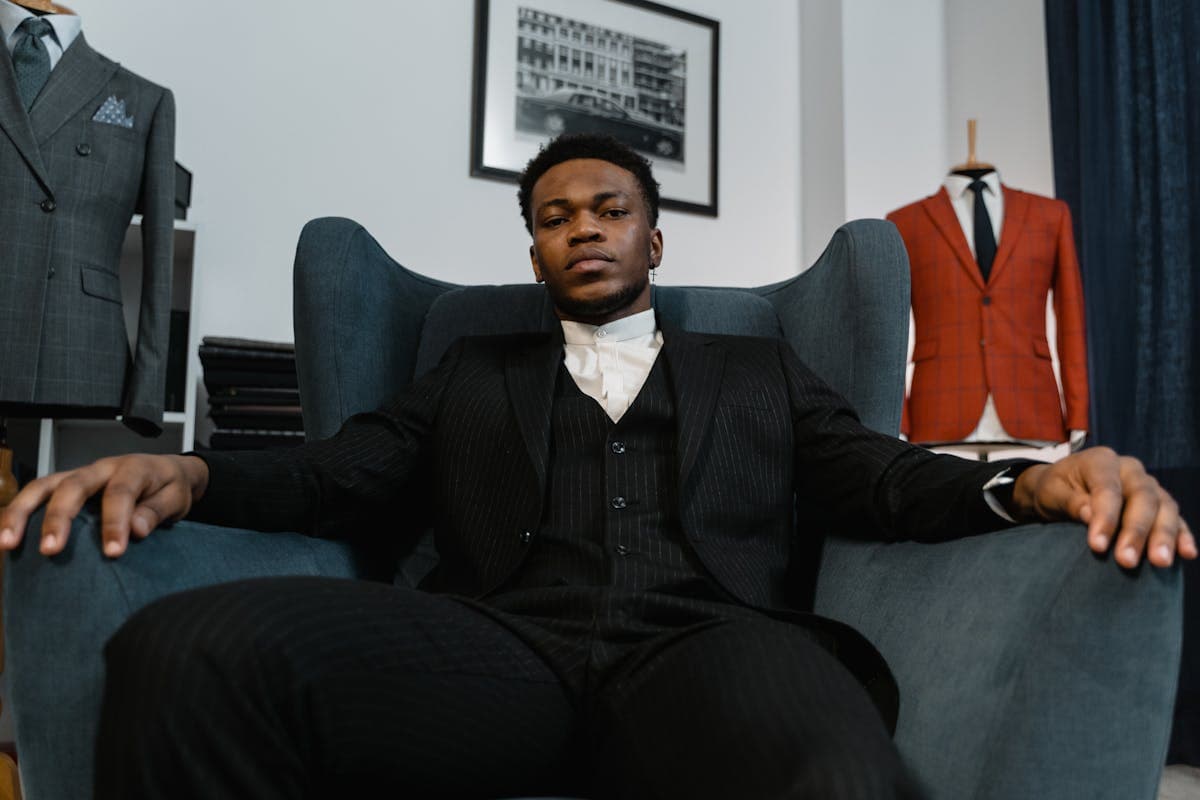 A sharply dressed man in a bold tailored suit with structured shoulders and wide lapels photographed against a plain backdrop