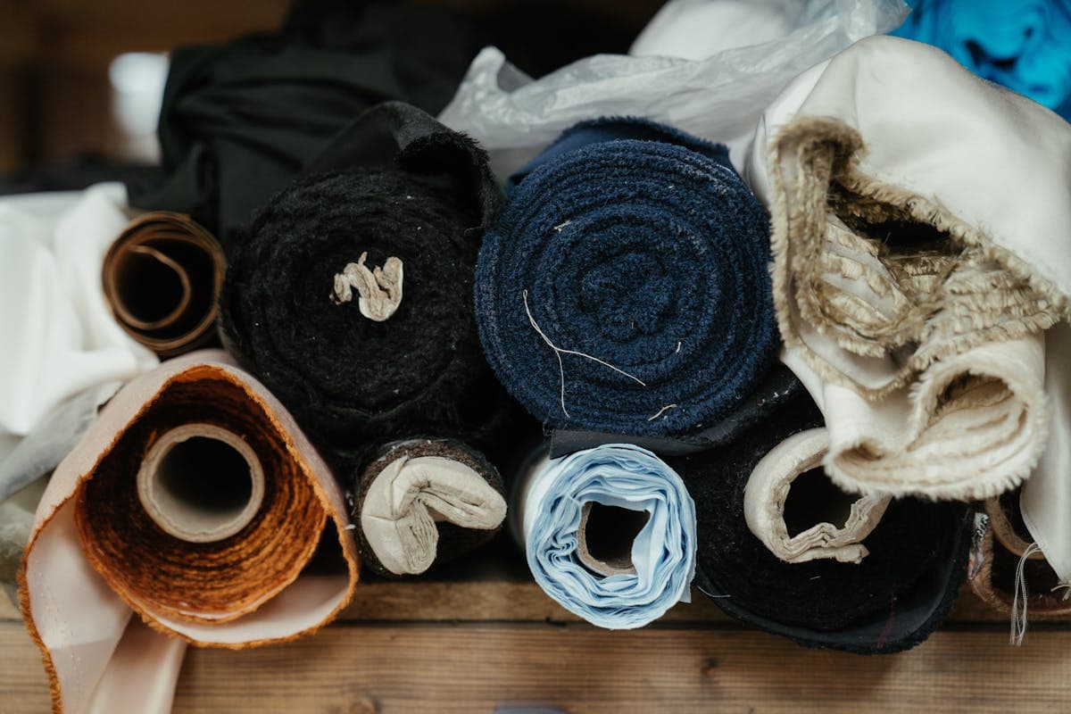 Bolts of cream and ivory wool suiting cloth on a tailor's workshop table, the kind of mill fabric a Hoi An tailor cuts a custom white suit from